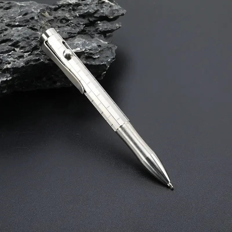 Bright silver titanium bolt action pen with the writing tip extended beside dark stone Main image