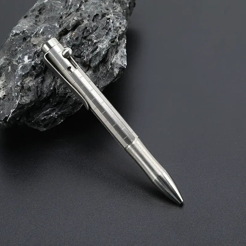 Silver titanium bolt action pen with the writing tip retracted, resting against dark stone