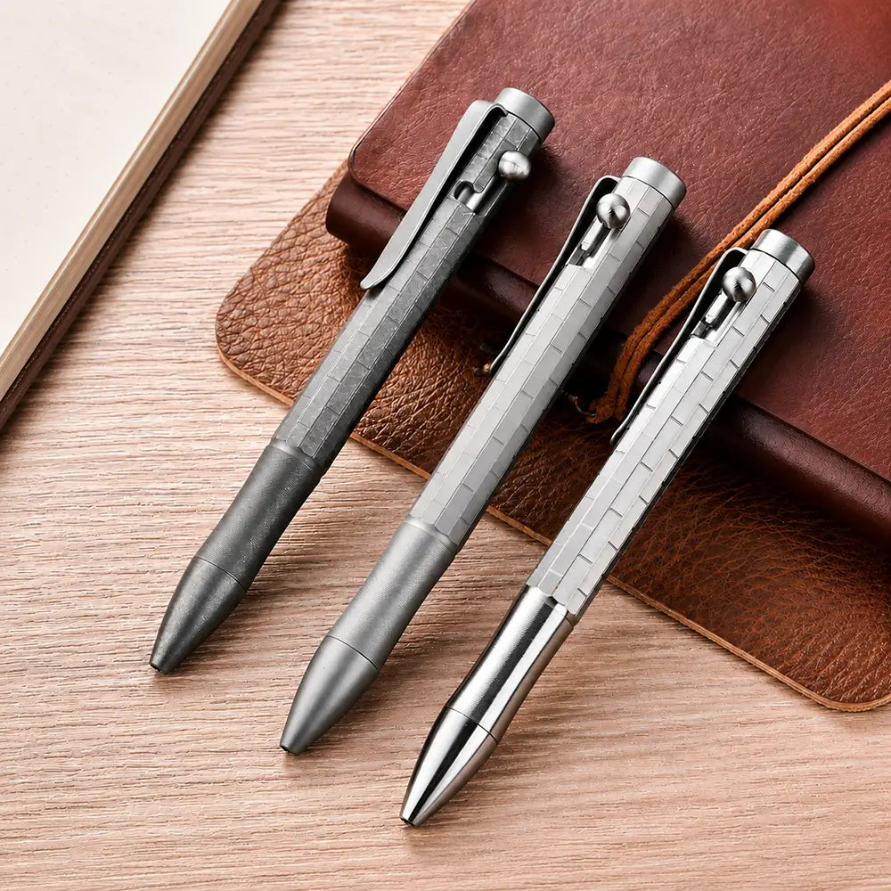Three titanium bolt action pens in natural, sandblasted and stonewashed finishes resting on leather notebooks